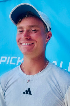 Person wearing a white Adidas shirt and cap against a blue background with 'PICK' branding.